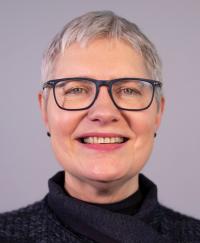 Dr Margot McCarthy. She is smiling, wearing glasses and a dark top
