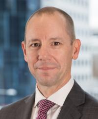 Randall Brugeaud. He is smiling wearing a dark jacket with red tie.
