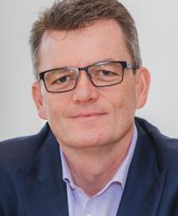 Andrew Colvin APM OAM. He is smiling, wearing glasses, a light shirt and navy blue sport coat.