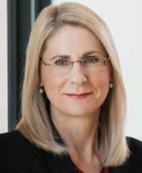 Dr Heather Smith PSM. She is smiling, wearing glasses and a dark jacket.