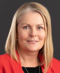 Mary Wiley-Smith. She is smiling wearing a dark blue top and red coat.