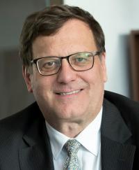 David Parker AM. He is smiling wearing glasses and a black suit.