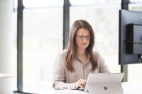 A woman with long brown hair looks at a lap top.