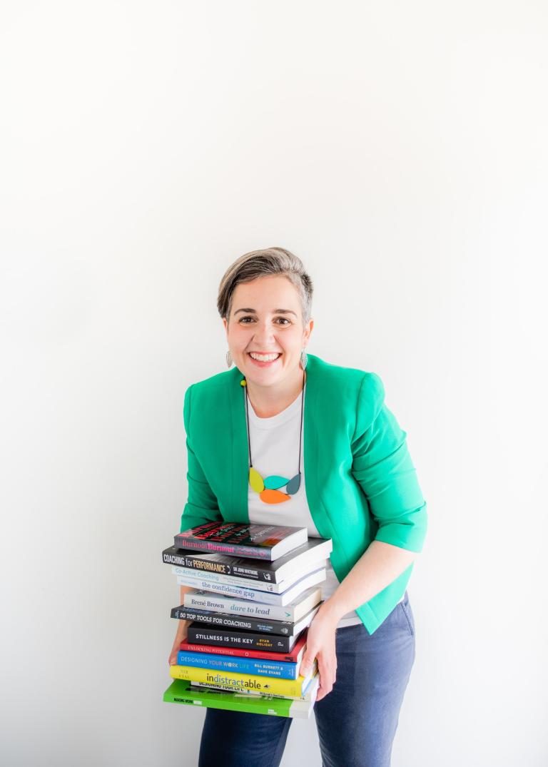 Portrait photo of Clare Conroy smiling while holding a large pile of books