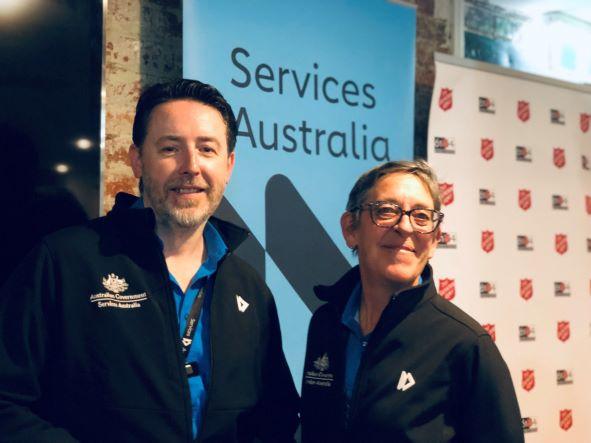 Photo in front of pull up banner of two people - CPSOs Nick and Rosemary - at the Community Partnership Pilot at Project 614, Salvation Army in Melbourne.