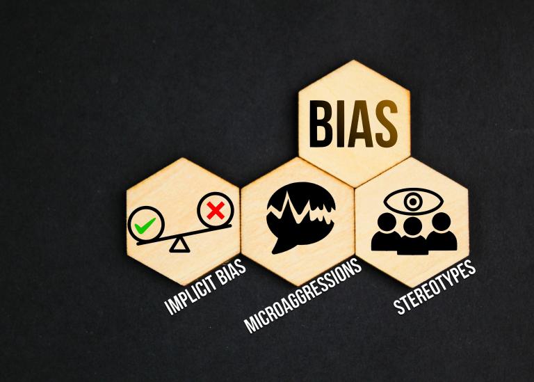Graphical illustration of 4 hexagons inside of which show the word, ‘Bias’, and a set of scales with ‘implicit bias’; a speech bubble cut in half with word ‘microaggressions’; 3 illustrative people with a thought bubble above them with the word ‘stereotypes’