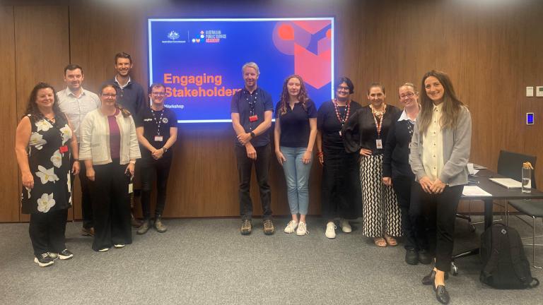 Photo of 10 people in a room looking at the camera in front of a screen with the APS Academy logo and Australian Government logo for the ‘Engaging Stakeholders’ course. 