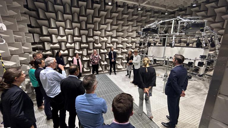 Photo inside the padded hearing test room at Cochlear with a number of policy officers and Cochlear staff observing the facility.