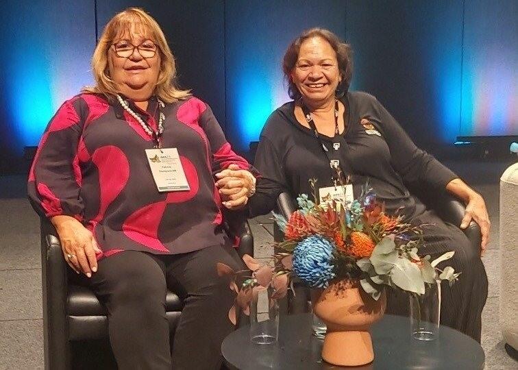 Photo of Patricia Thompson AM and Raelene Rosas seated on stage at the 2024 Australian Evaluation Society International Evaluation Conference shortly before presenting.