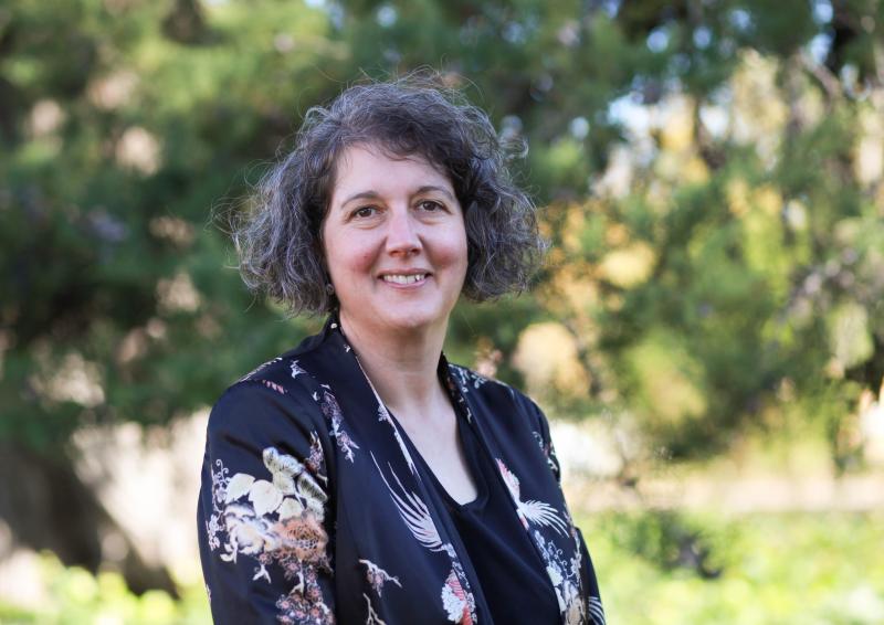 A headshot of Jaala Hinchcliffe, Integrity Commissioner and Integrity Faculty. Jaala is wearing a navy floral jacket and standing outside. There are green leafy trees in the background.