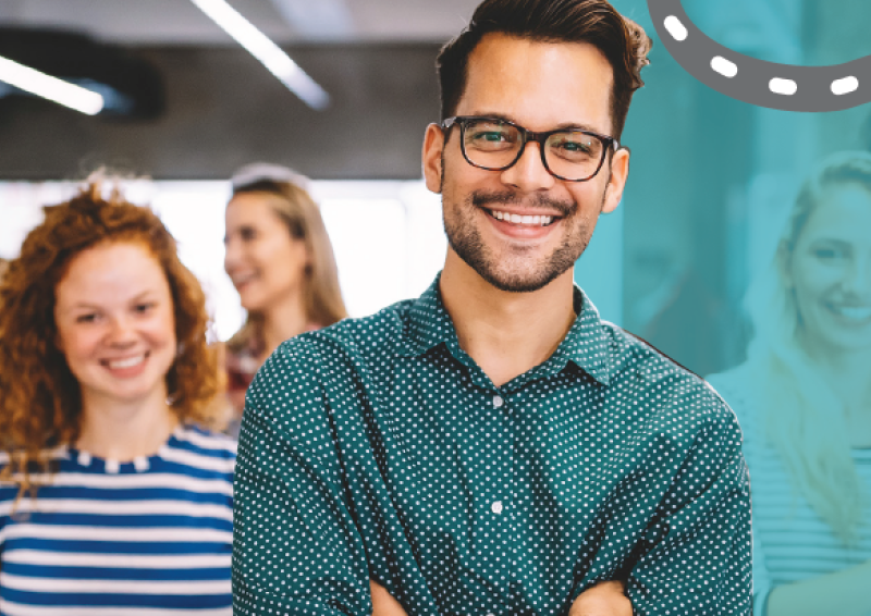 A student wearing glasses and casual clothes, smiling, with five more happy students in background
