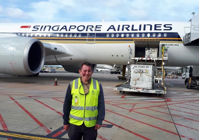 A man, Eamon Lindsay, in high visibility vest standing in front of a plane having cargo loaded.