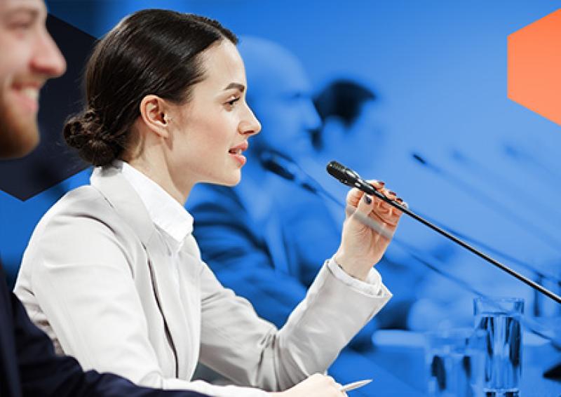 Two people sitting at a desk in front of a microphone
