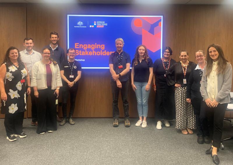 Photo of 10 people in a room looking at the camera in front of a screen with the APS Academy logo and Australian Government logo for the ‘Engaging Stakeholders’ course.