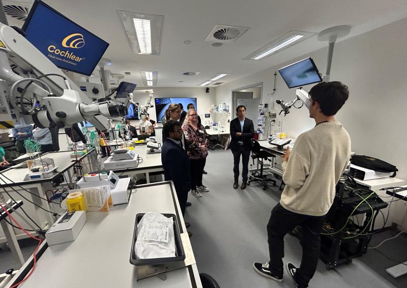 Image of desks and technical equipment and a Cochlear operator talking to 4 policy officers