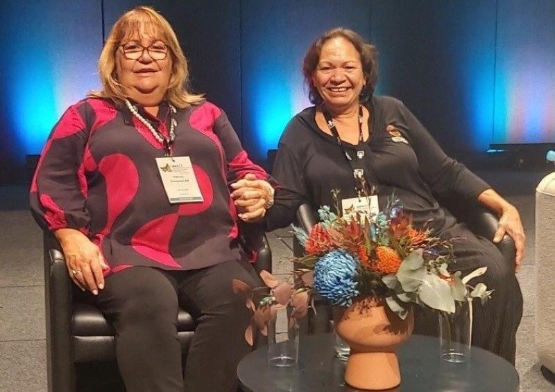Photo of Patricia Thompson AM and Raelene Rosas seated on stage at the 2024 Australian Evaluation Society International Evaluation Conference shortly before presenting.