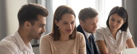 Two women and two men looking at two computer screens in a work environment.