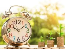 Image of clock with 3 adjacent coin stacks with green plants growing out of them.