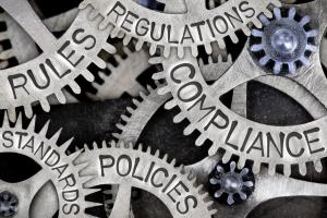Interlocking cogs with the words rules, regulations, standards, compliance and policies written on the cogs.