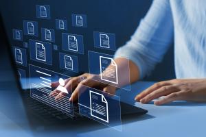 Illustrative image of person’s hands at laptop with overlay of document icons hovering in mid air in front of the person.