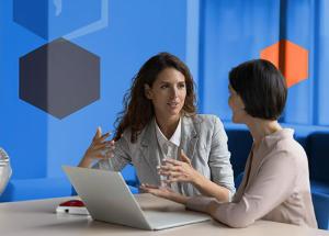Two people sitting and conversing in front of an open laptop