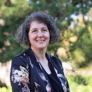 A headshot of Jaala Hinchcliffe, Integrity Commissioner and Integrity Faculty. Jaala is wearing a navy floral jacket and standing outside. There are green leafy trees in the background. 