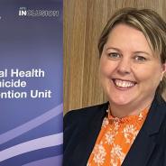 Rachael McMahon in front of a banner for  the APS Mental Health and Suicide Prevention Unit