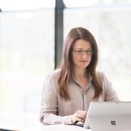 A woman with long brown hair looks at a lap top. 