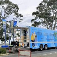 Image of Services Australia bus parked by side of road with picture of three people painted on its side with blue gum tree leaves on the background.