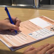A kitchen bench top with a visual of a left hand writing on a paper form with a pen.