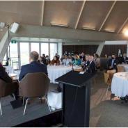 Members of the national regulators community of practice sitting at 4 dining tables listening to a panel discussion.