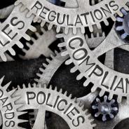 Interlocking cogs with the words rules, regulations, standards, compliance and policies written on the cogs.