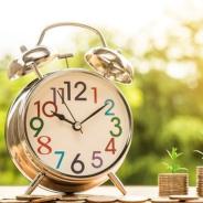 Image of clock with 3 adjacent coin stacks with green plants growing out of them.