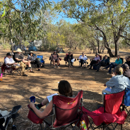 Photo of people sitting around on camp chairs in a circle in a open bushland setting.