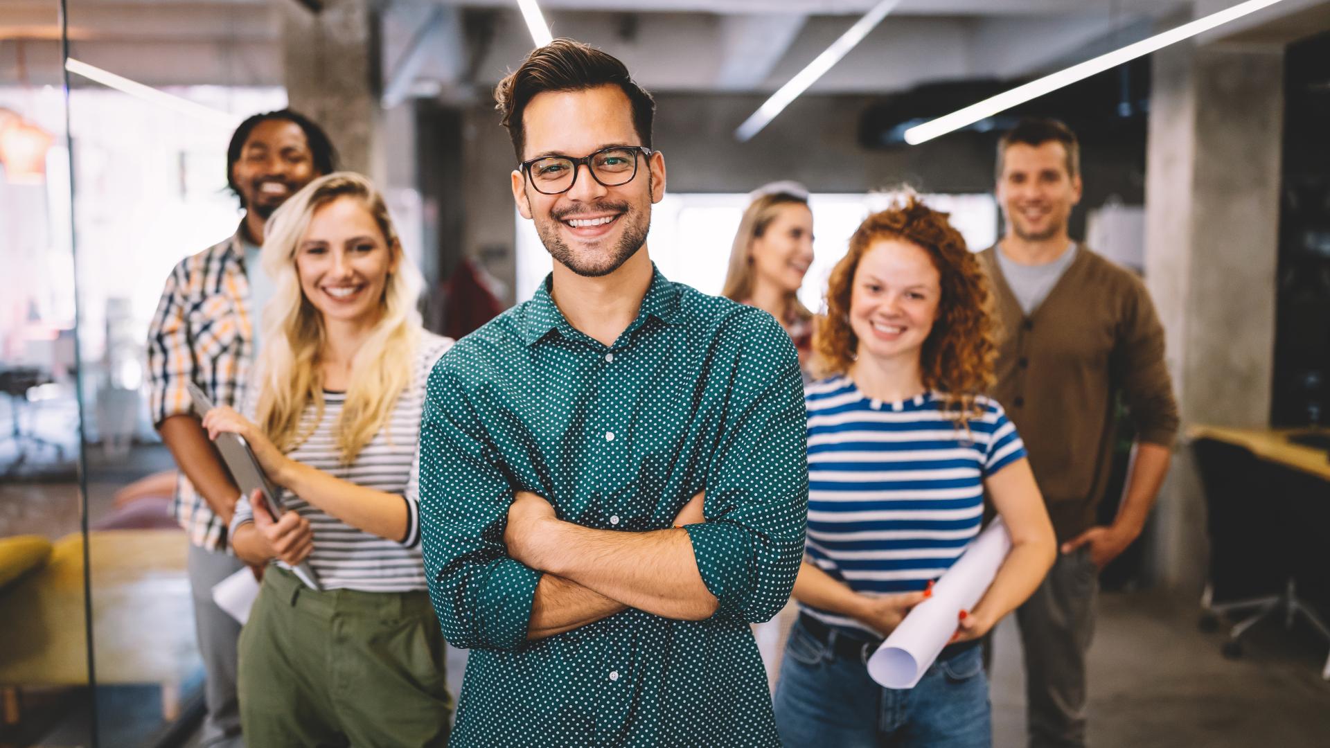 A student wearing glasses and casual clothes, smiling with six more happy students in background