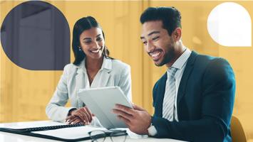 Two people sitting and smiling, looking at laptop screen.