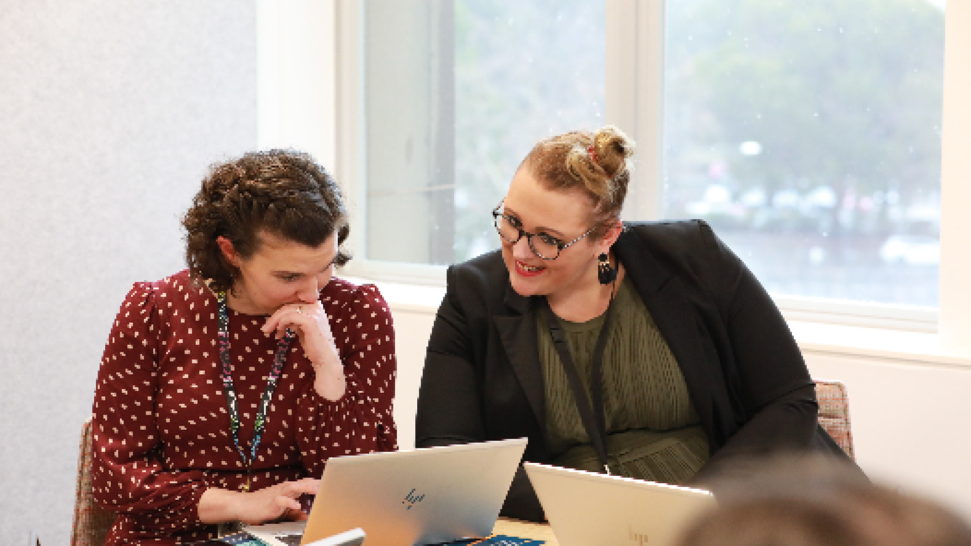 Two people sitting at a meeting table with laptops open and looking intently at the laptop screeen.