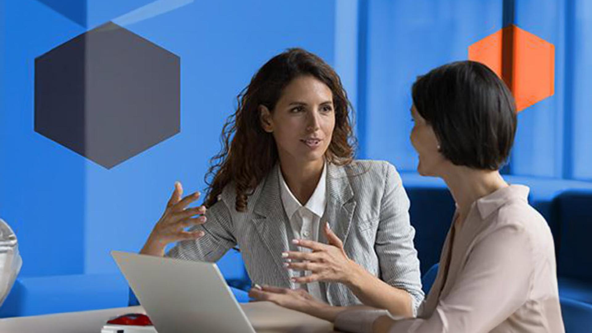 Two people sitting and conversing in front of an open laptop