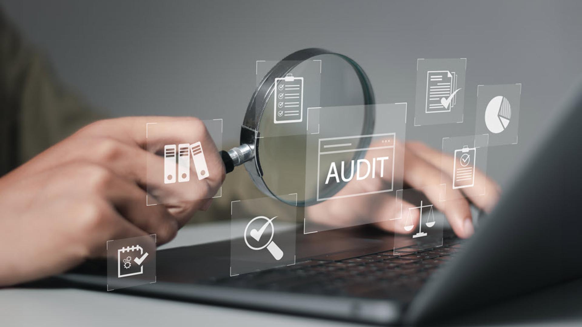 Illustrative image of person’s hand holding magnifying glass in front of a laptop with some floating graphics of checklist, word AUDIT, pie chart and folders