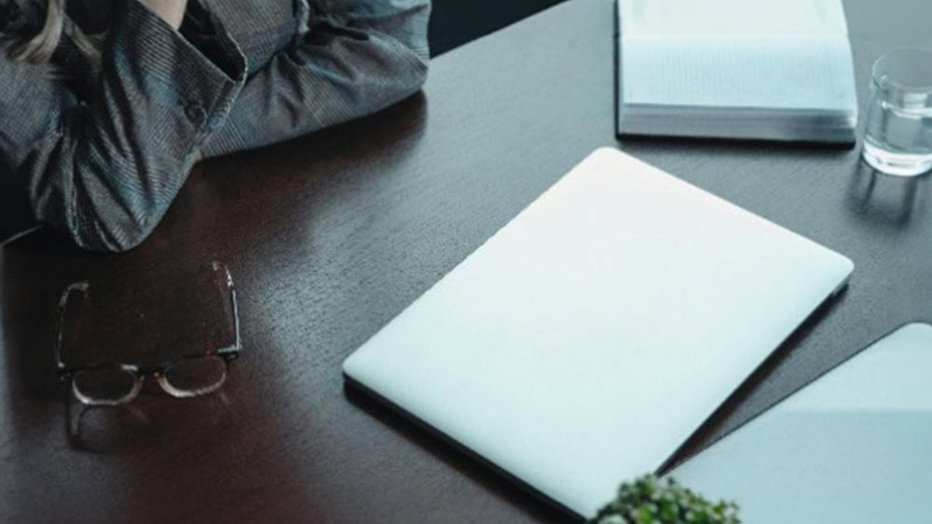 Image of person sitting a desk with a closed laptop, glasses resting on the desk and an open diary