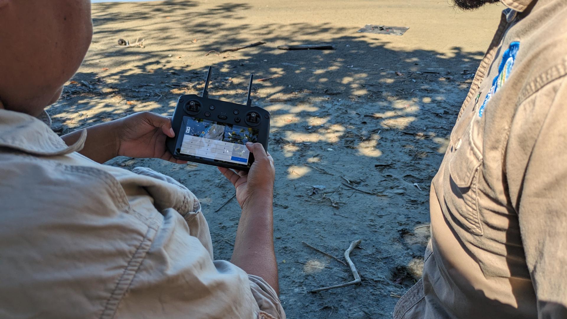 Image of two First Nations men standing on Larrakia land piloting a drone through a handheld device.