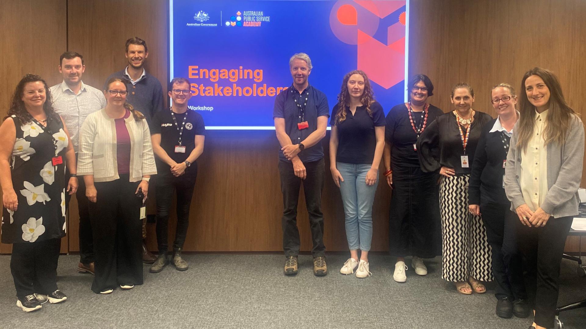 Photo of 10 people in a room looking at the camera in front of a screen with the APS Academy logo and Australian Government logo for the ‘Engaging Stakeholders’ course. 