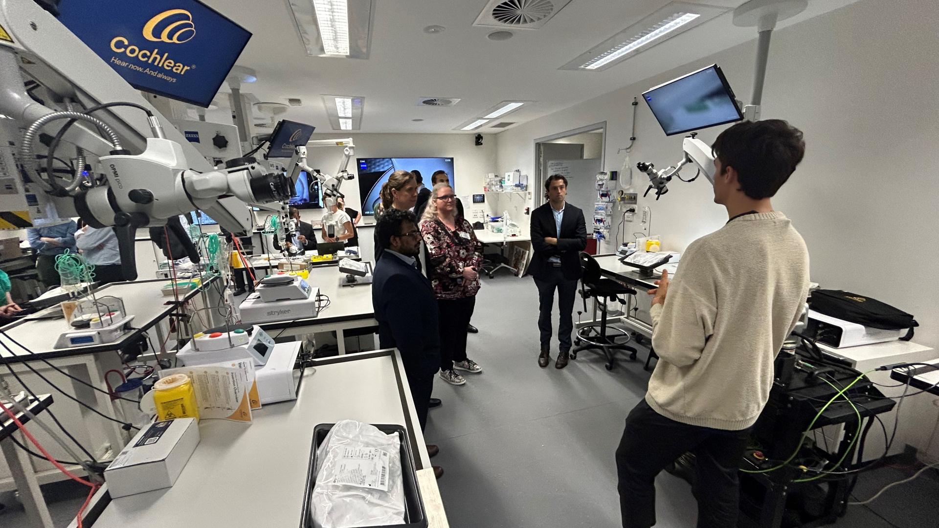 Image of desks and technical equipment and a Cochlear operator talking to 4 policy officers 