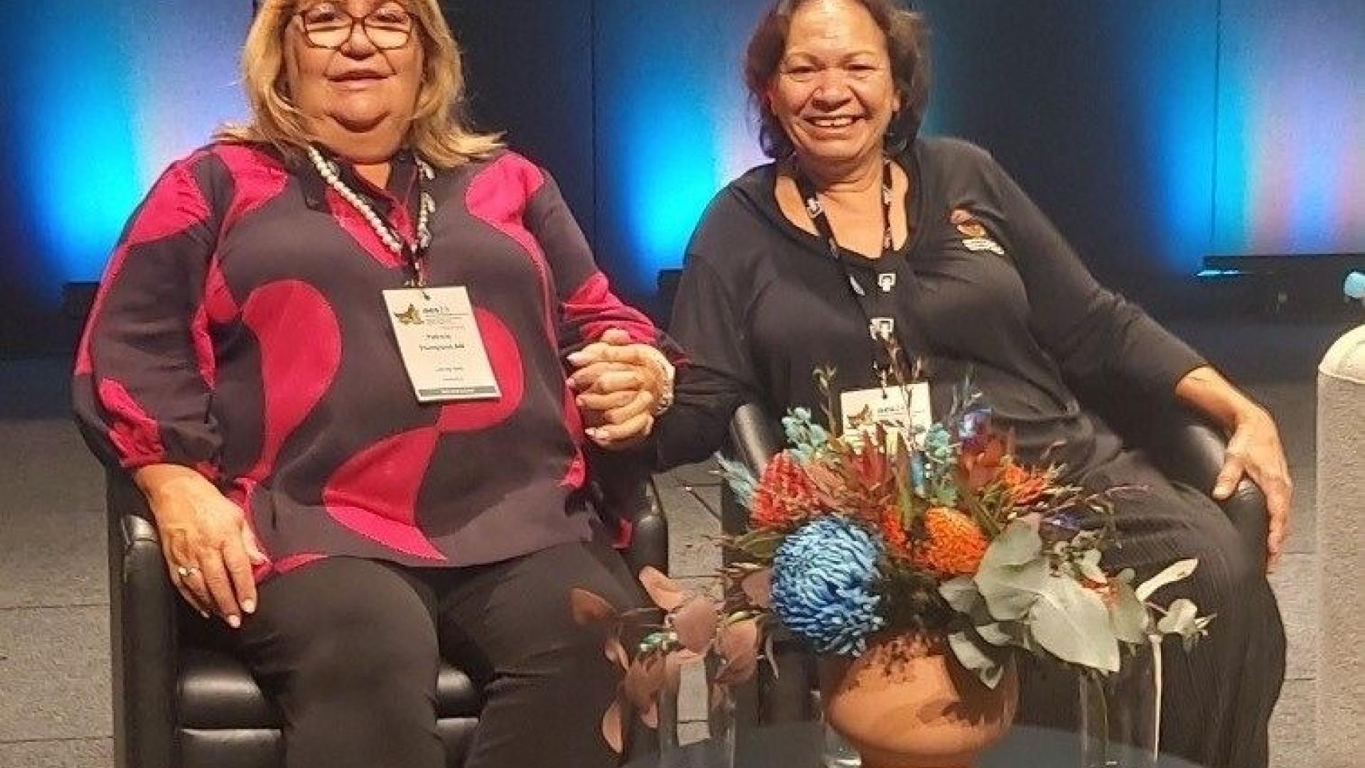 Photo of Patricia Thompson AM and Raelene Rosas seated on stage at the 2024 Australian Evaluation Society International Evaluation Conference shortly before presenting. 