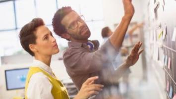 An image of a man and a woman in front of a whiteboard looking at it.  