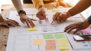 A UX design team is a confluence of user research, UX, UI design with layout paper on desk.