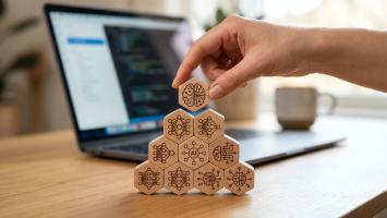 Hand carefully places a hexagonal wooden piece on a growing structure, symbolizing strategic development and problem-solving in a modern technology and coding environment
