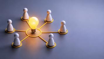 Connected people surrounding a glowing light bulb, knowledge sharing and team collaboration concept