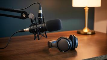 Podcast microphone and headphones set up on wooden desk with lamp in background symbolizing audio recording and content creation for broadcasting and sound production