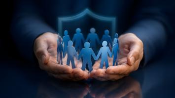 Hands holding paper figures with a glowing blue shield representing protection